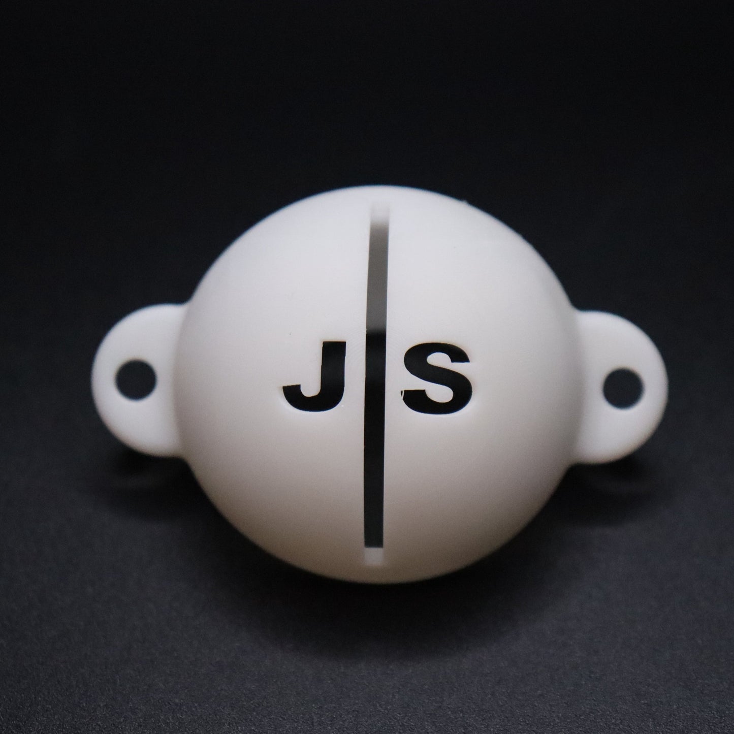 Golf ball marker stencil manufactured via 3D printing in white plastic material. Two letters for initials, one on each side of an alignment line for putting